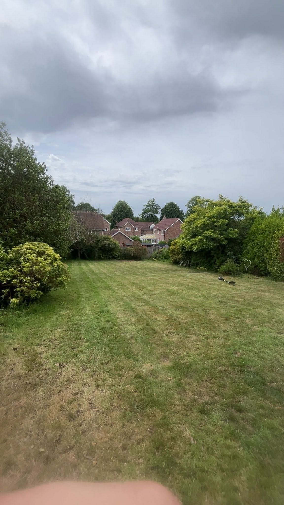 Large residential brick house in distance with green lawn and surrounding trees under overcast sky