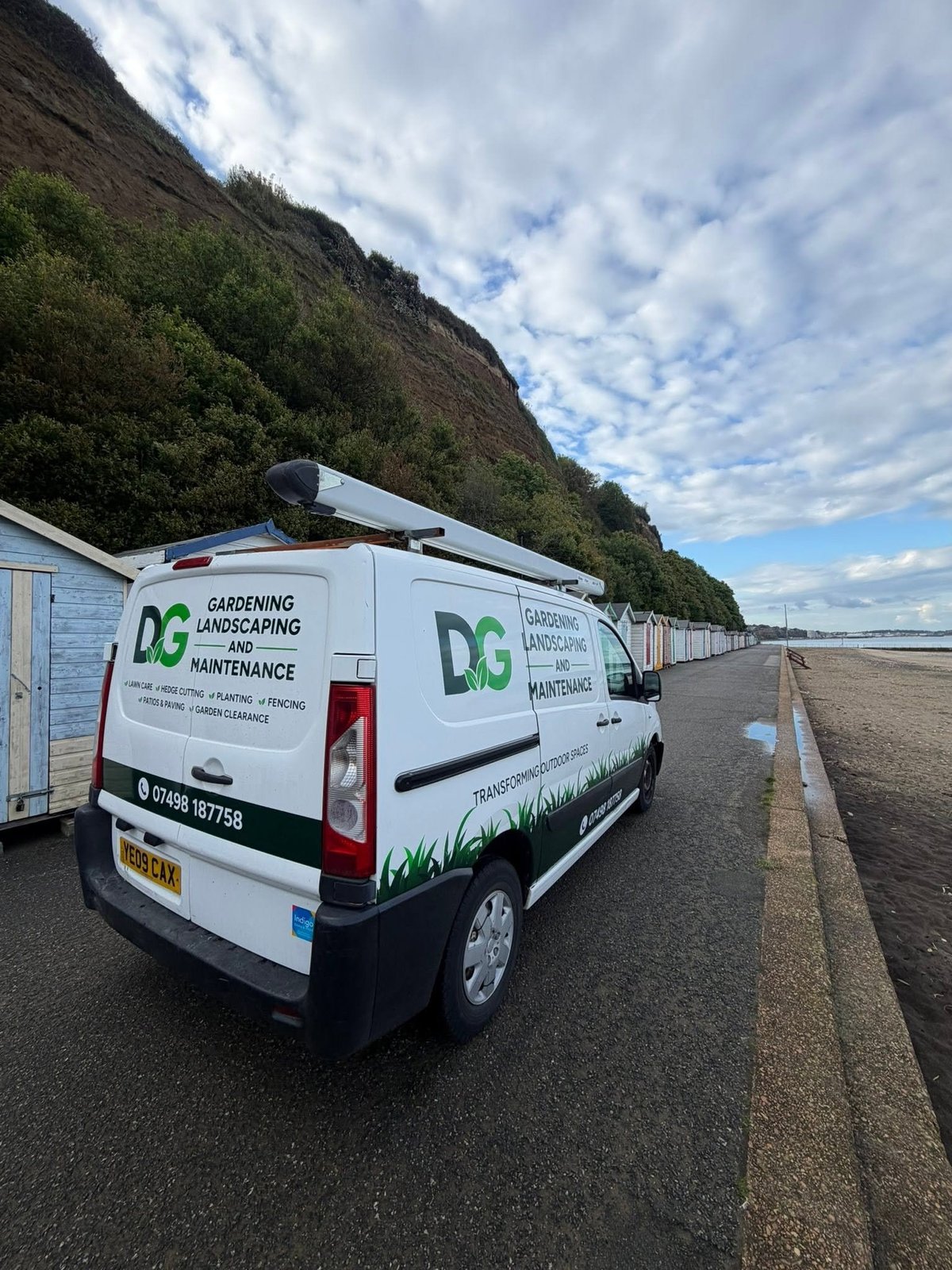 White van with DG Gardening, Landscaping and Maintenance branding parked on a road with grassy cliff and sky