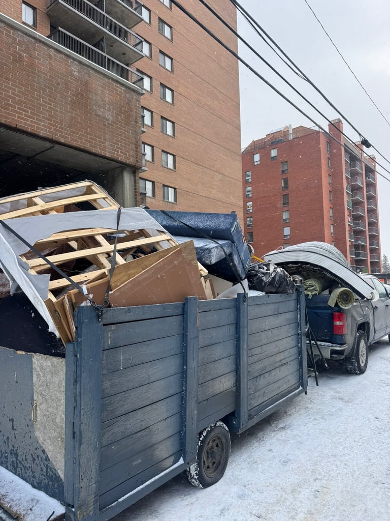 Overloaded blue pickup truck with wooden debris parked in front of brick apartment buildings