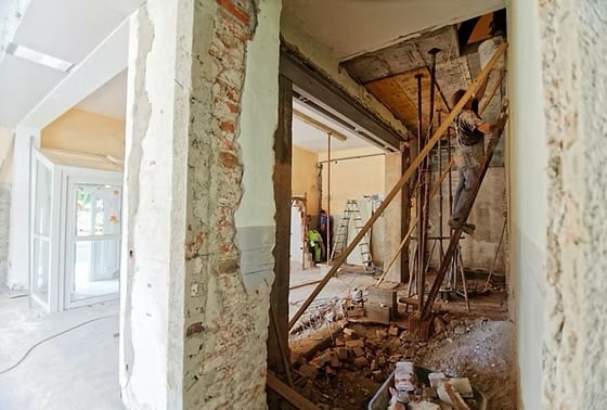 Interior renovation in progress by Holsclaw Building — exposed brick walls, structural framing, and construction materials visible in the adjoining room