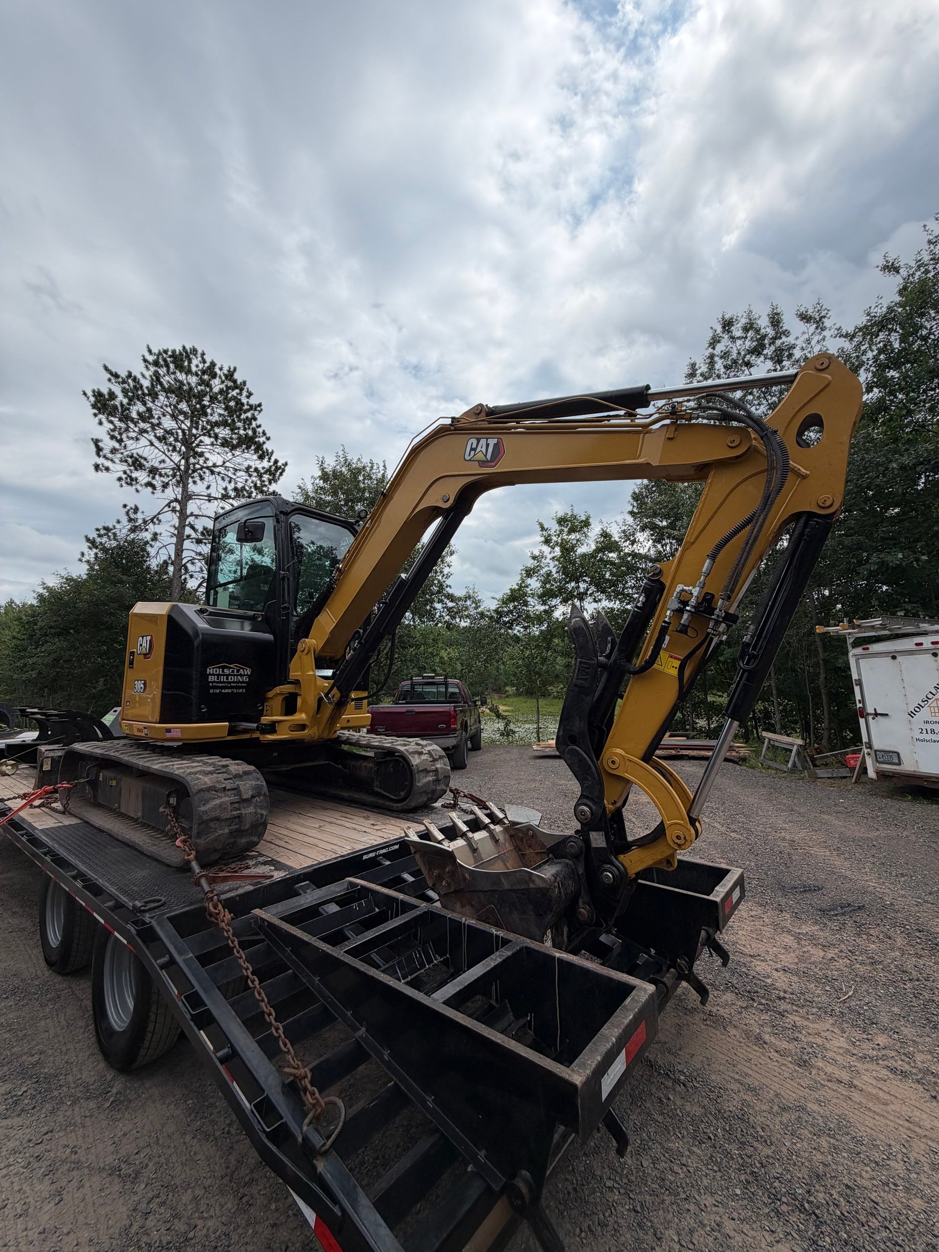 Holsclaw Building CAT 305 compact excavator with the Holsclaw Building & Property Services logo, loaded on a flatbed trailer at the equipment yard