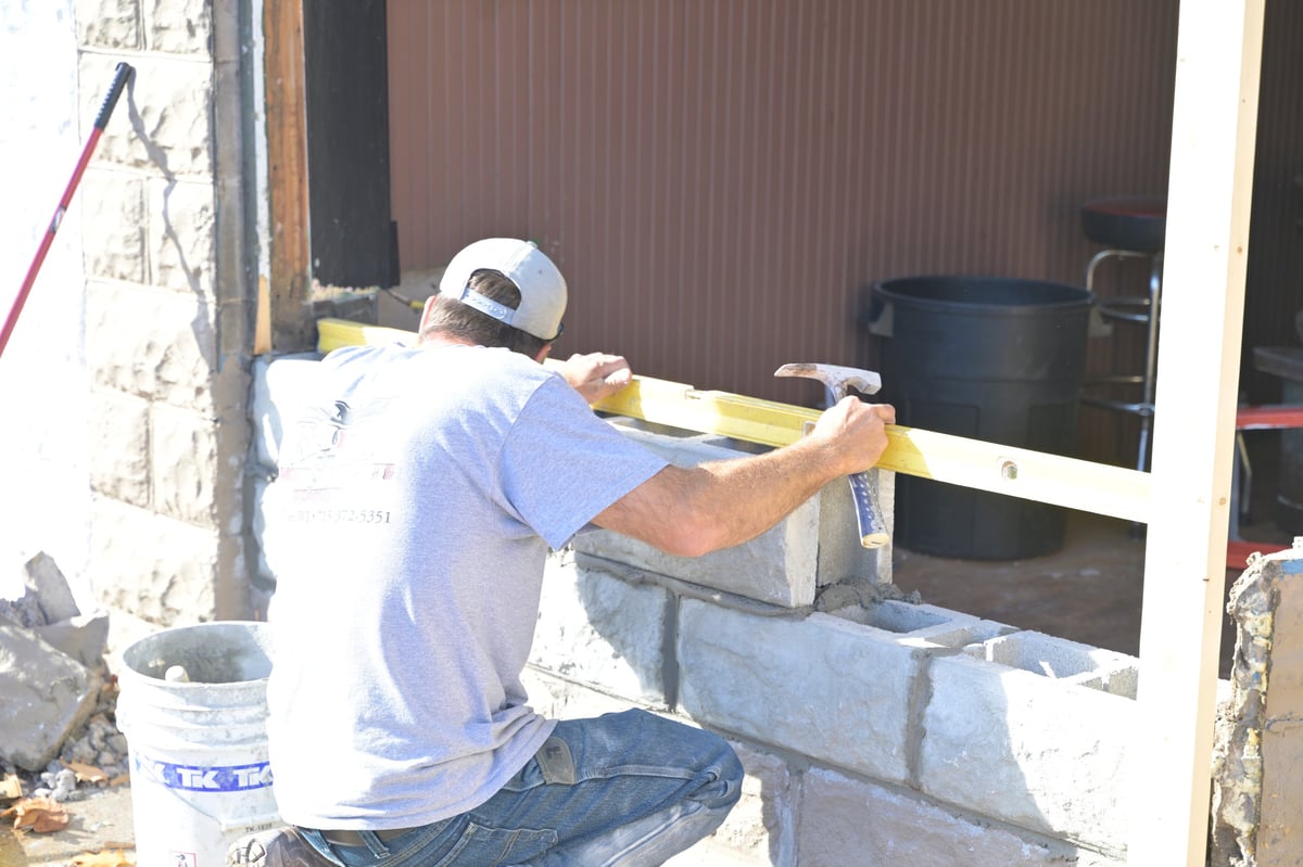 Holsclaw Building construction worker wearing a white hard hat uses a level to check alignment on a block wall during the brewery repair
