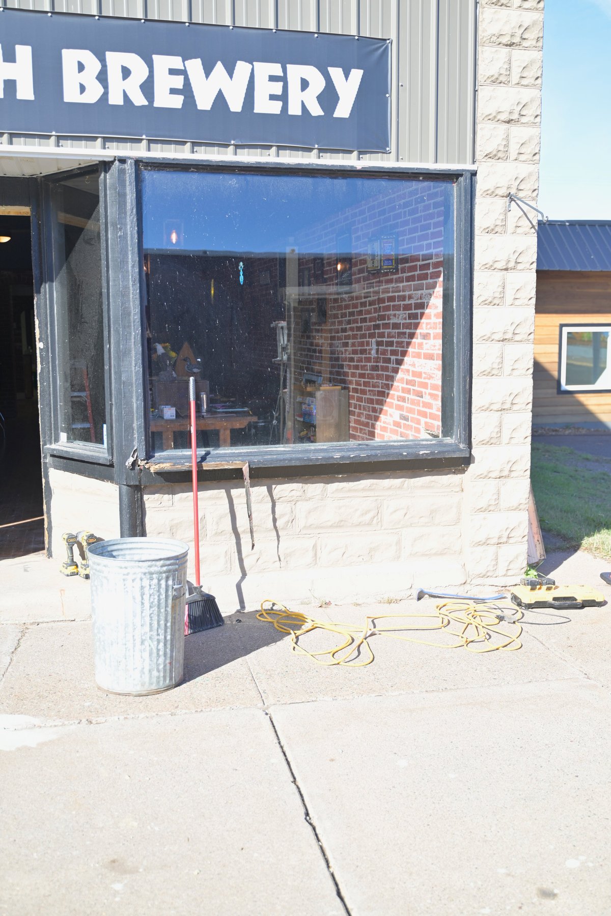 Exterior bay window of Raven's Breath Brewery under repair with blue signage, exposed framing, and construction equipment on the sidewalk