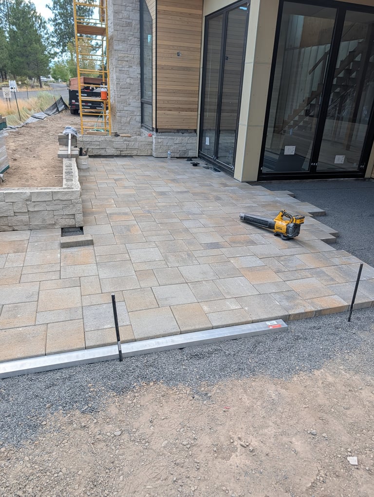 Patio under construction with paver installation, modern home exterior, and construction equipment visible