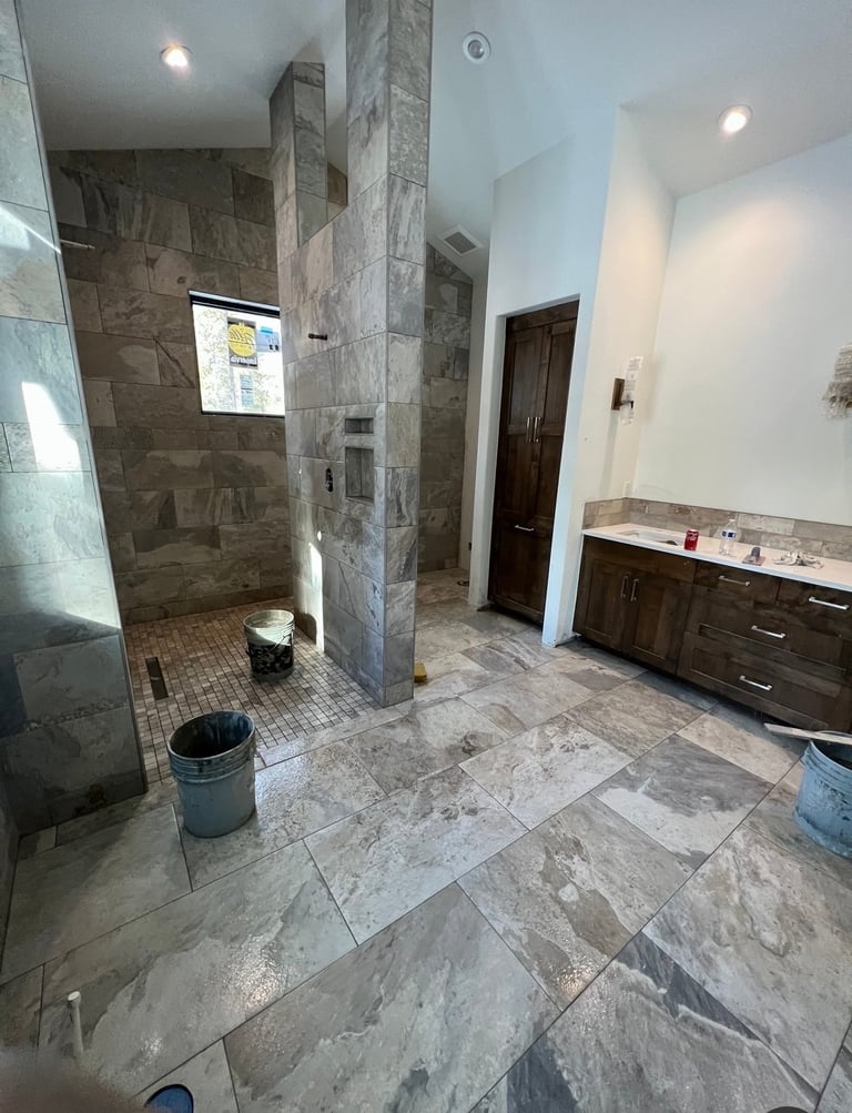 Modern bathroom under renovation with marble tile flooring, walk-in shower, dark vanity cabinet, and construction materials