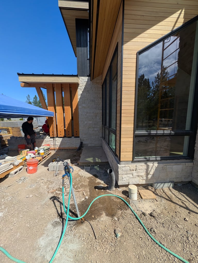 Construction site at modern home with turquoise hose, wooden architectural elements, and workers in background on sunny day