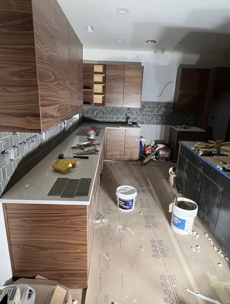 Kitchen under renovation with wood cabinets, tile backsplash, concrete floor, and construction materials scattered throughout