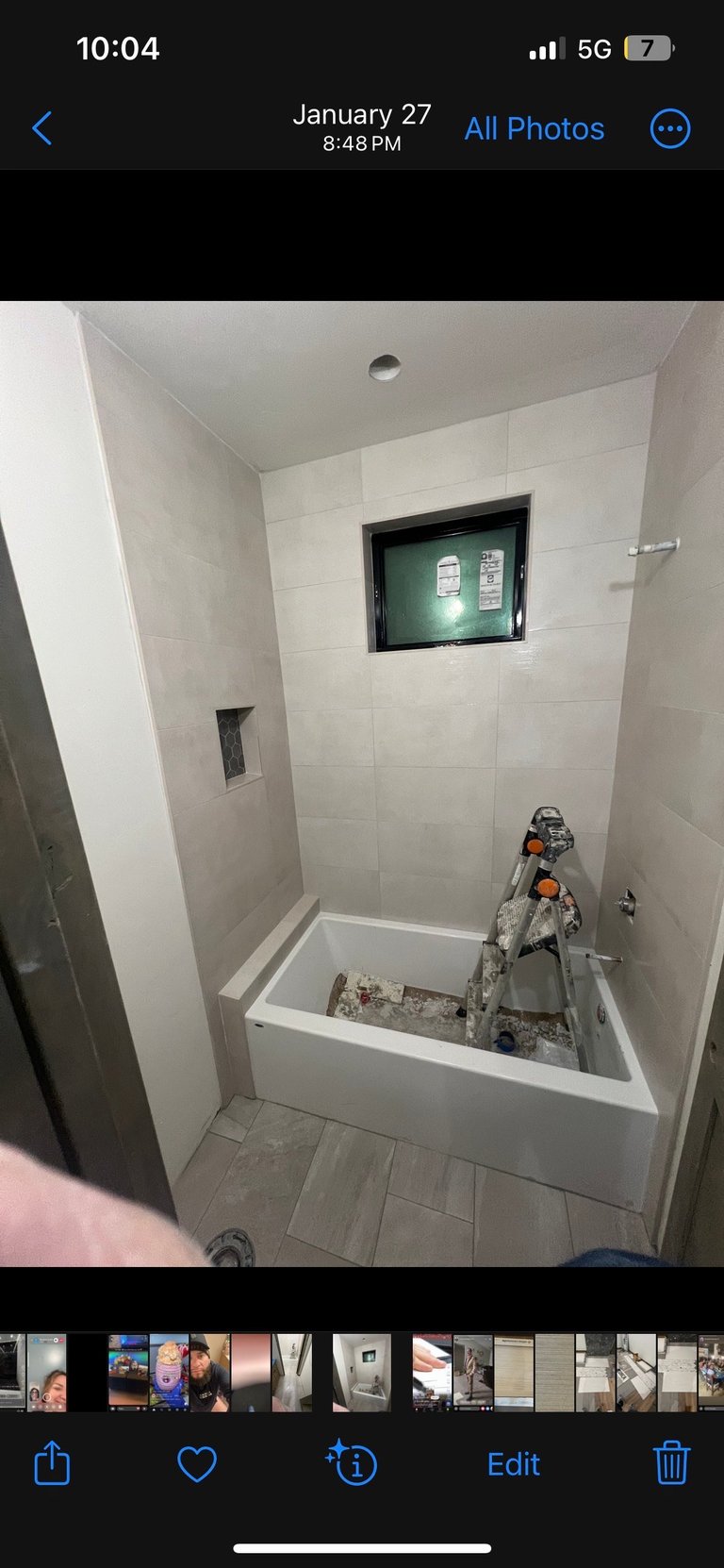 Bathroom shower installation in progress with white tile walls, an inset niche, and construction tools inside the tub
