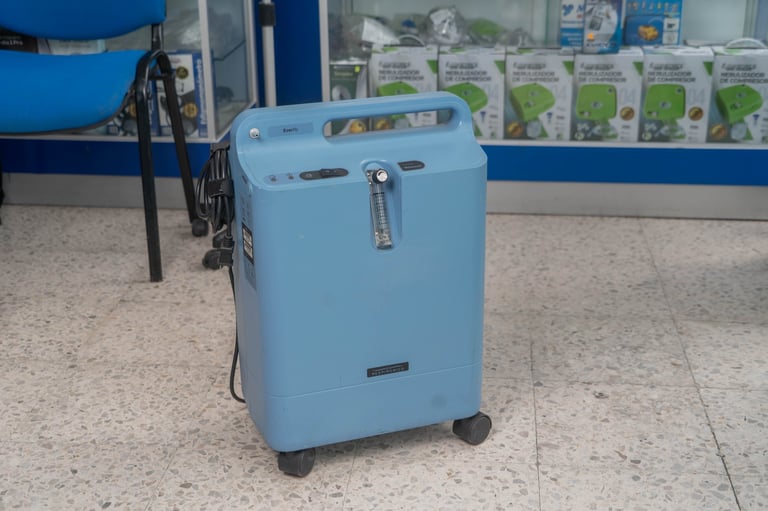 Light blue oxygen concentrator machine on wheels in a medical or clinical setting with shelves of supplies in the background