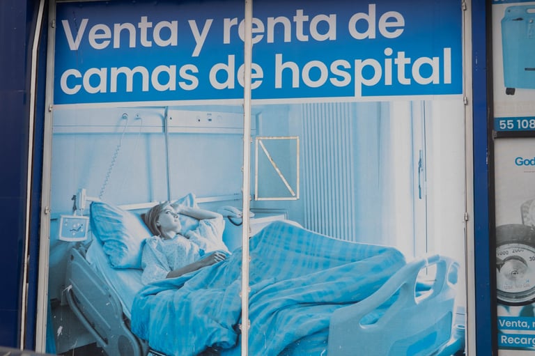 Store window displaying hospital bed for sale or rent with blue bedding and blue header text in Spanish