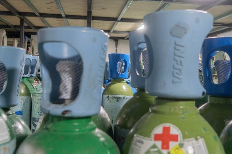 Industrial gas cylinders with blue caps lined up in a warehouse, featuring green tanks with medical cross labels and branding text