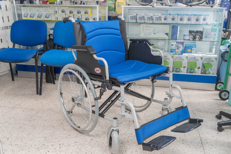 White and blue manual wheelchair with footrest in a medical office waiting area with blue chairs and storage shelves.
