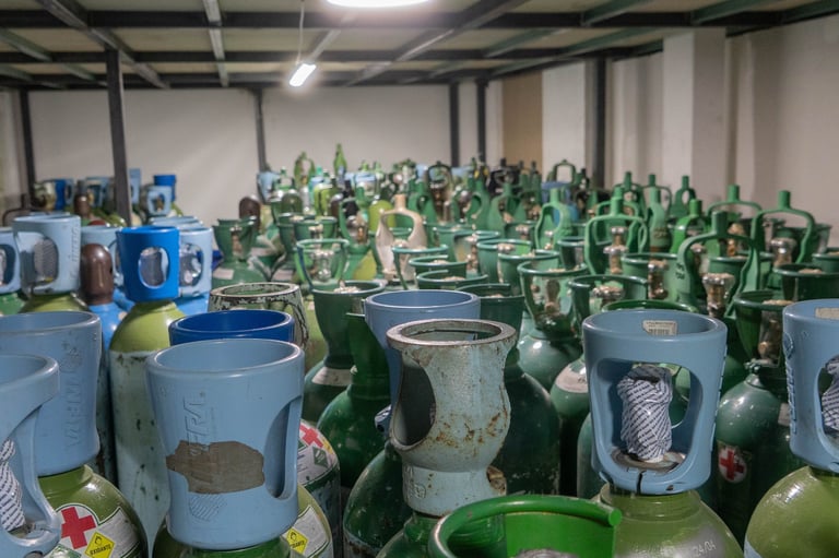 Rows of green and blue propane cylinders stored in an industrial warehouse facility with fluorescent ceiling lights