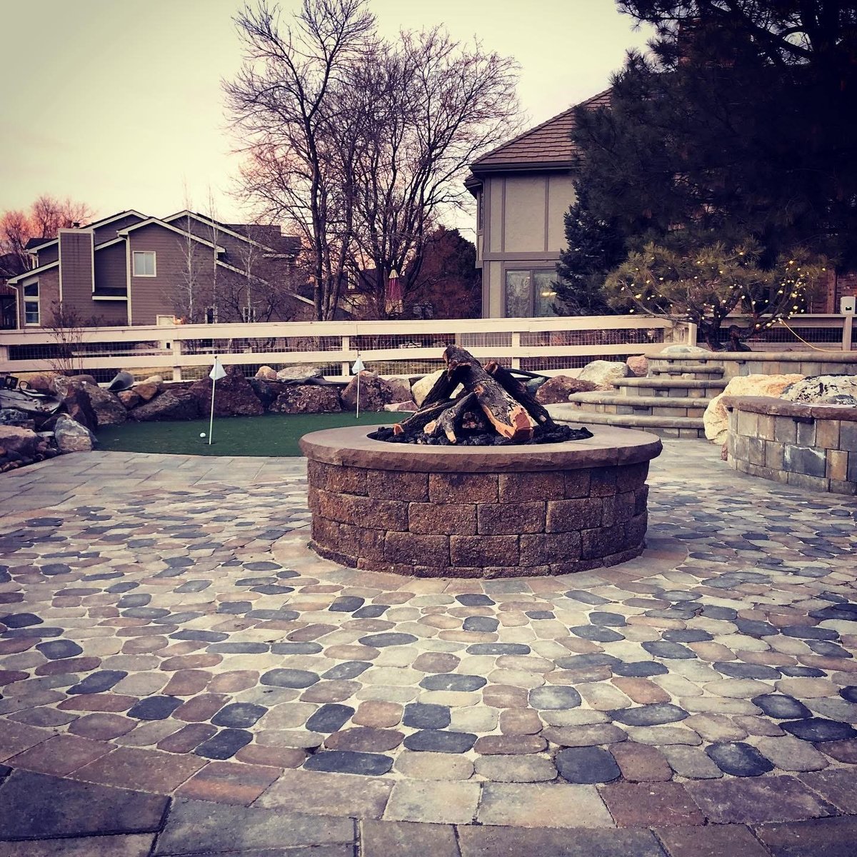 Backyard patio with circular stone fire pit, decorative paver surface, bare trees, and residential buildings