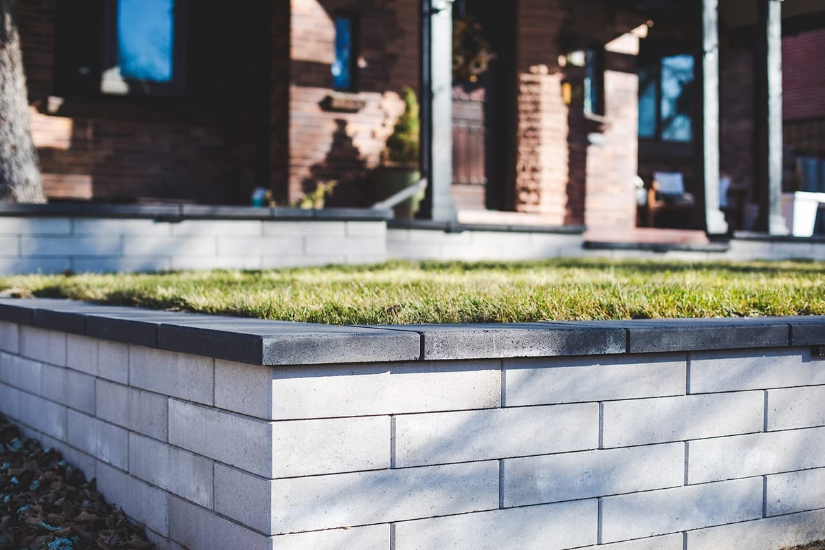 Raised garden bed with green grass and white brick planter in front of modern residential building