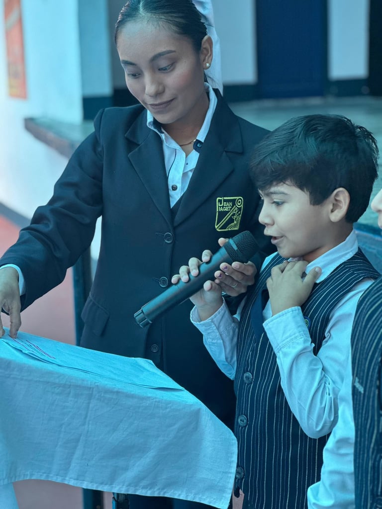 Woman teacher in blazer helps young boy in formal wear examine blue fabric through magnifying glass in classroom setting