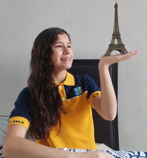 Girl in yellow and blue polo shirt holding a small Eiffel Tower model on her hand, smiling at camera