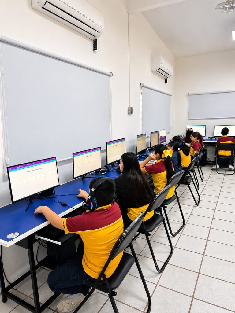 Students in yellow and maroon uniforms working at computer stations in a classroom with whiteboard walls and air conditioning units.