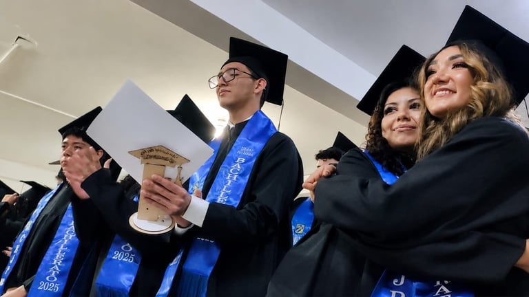 Group of graduates in black caps and gowns with blue sashes celebrating at commencement ceremony
