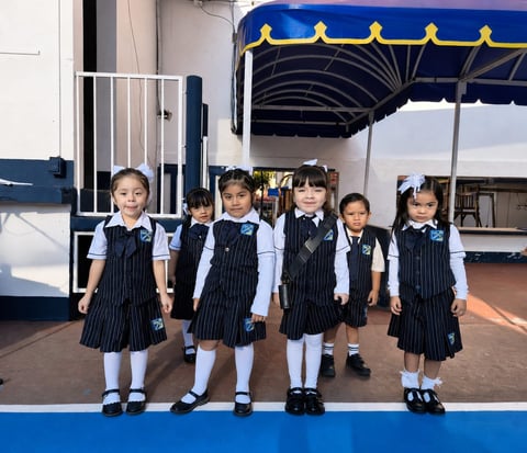 Six young students in navy pinstriped school uniforms standing in a line on a blue stage under a blue and yellow awning.
