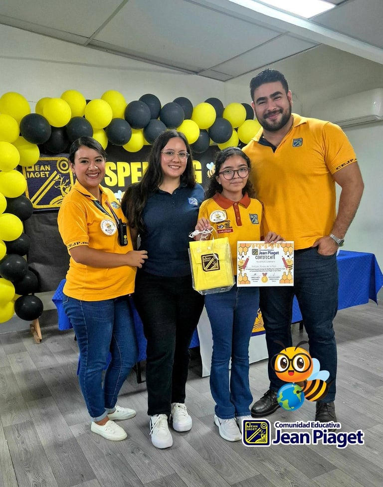 Four people in yellow and black uniforms posing with awards at a Jean Piaget event, with yellow and black balloon decorations in background