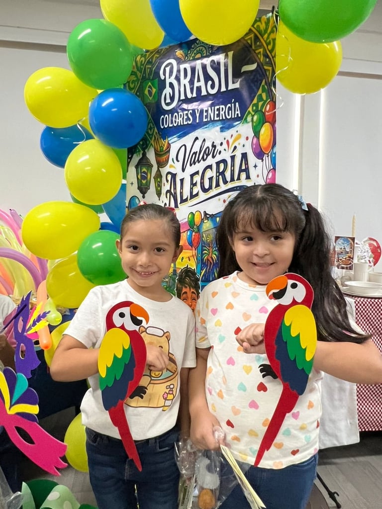 Two young girls smiling at a Brazilian-themed party with colorful balloons and festive decorations behind them