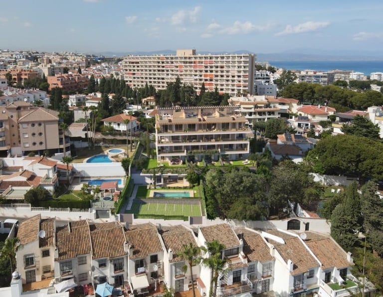 Aerial view of Mediterranean coastal town with white villas, modern apartment buildings, swimming pools, and sea in background