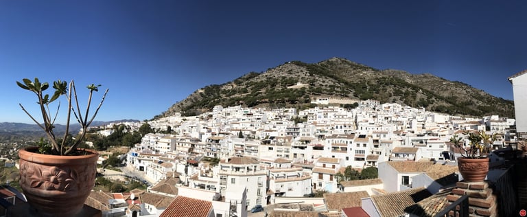 Whitewashed hillside town with densely packed buildings cascading down a rocky mountain under clear blue sky