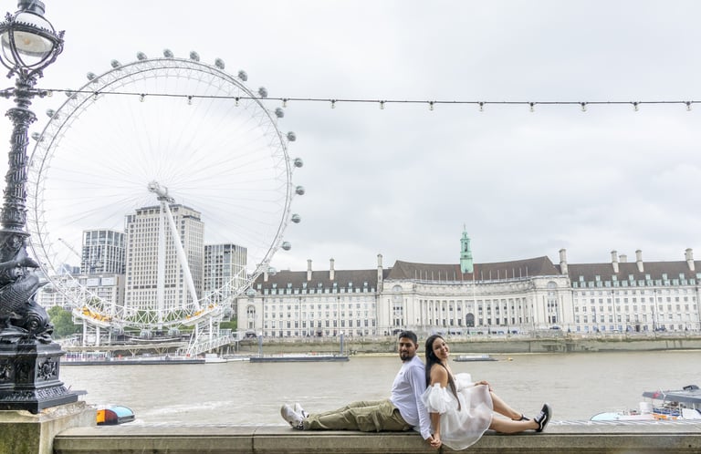 Couple sitting by Thames River with London Eye ferris wheel and historic riverside buildings in background