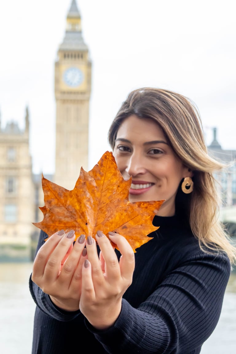 Woman holding a golden autumn leaf with Big Ben and London cityscape in the background
