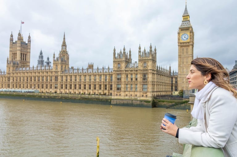 Woman holding a blue coffee cup viewing Big Ben and the Houses of Parliament across the Thames River in London