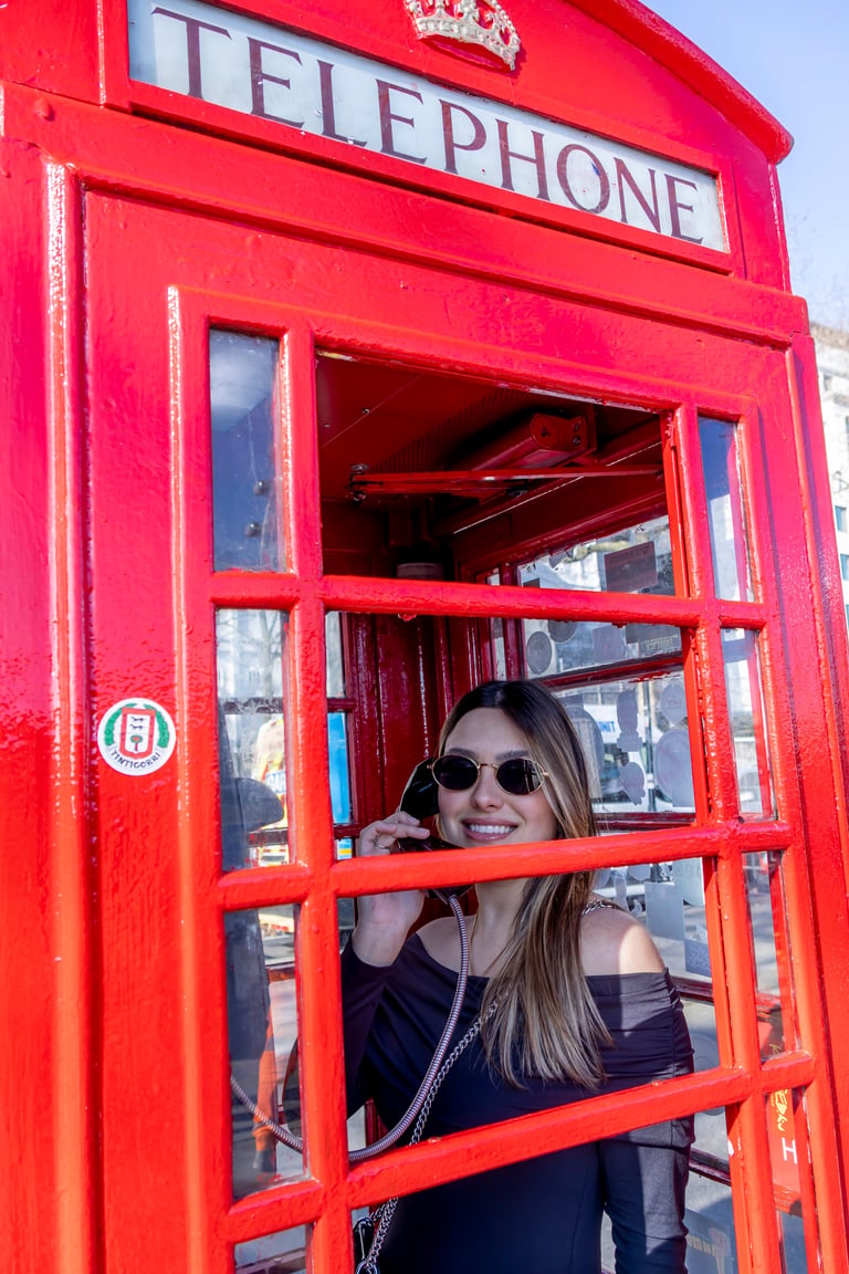 Woman wearing sunglasses smiling inside a classic red British telephone booth