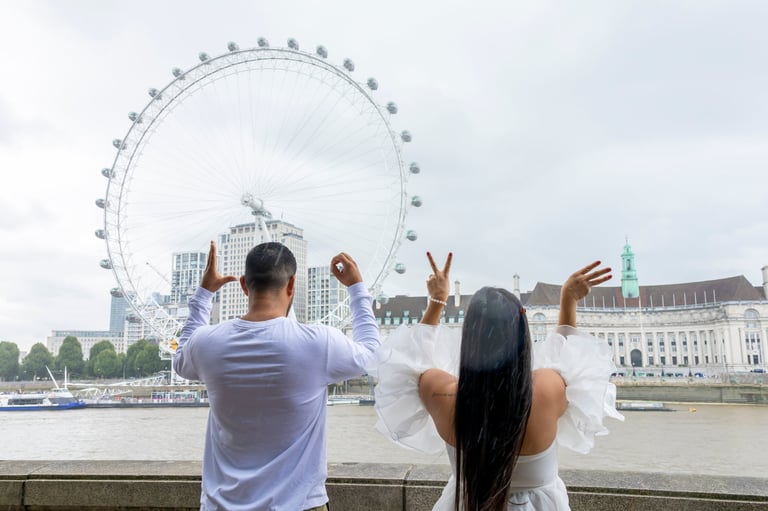 Couple posing playfully in front of London Eye, making peace signs with River Thames and cityscape in background