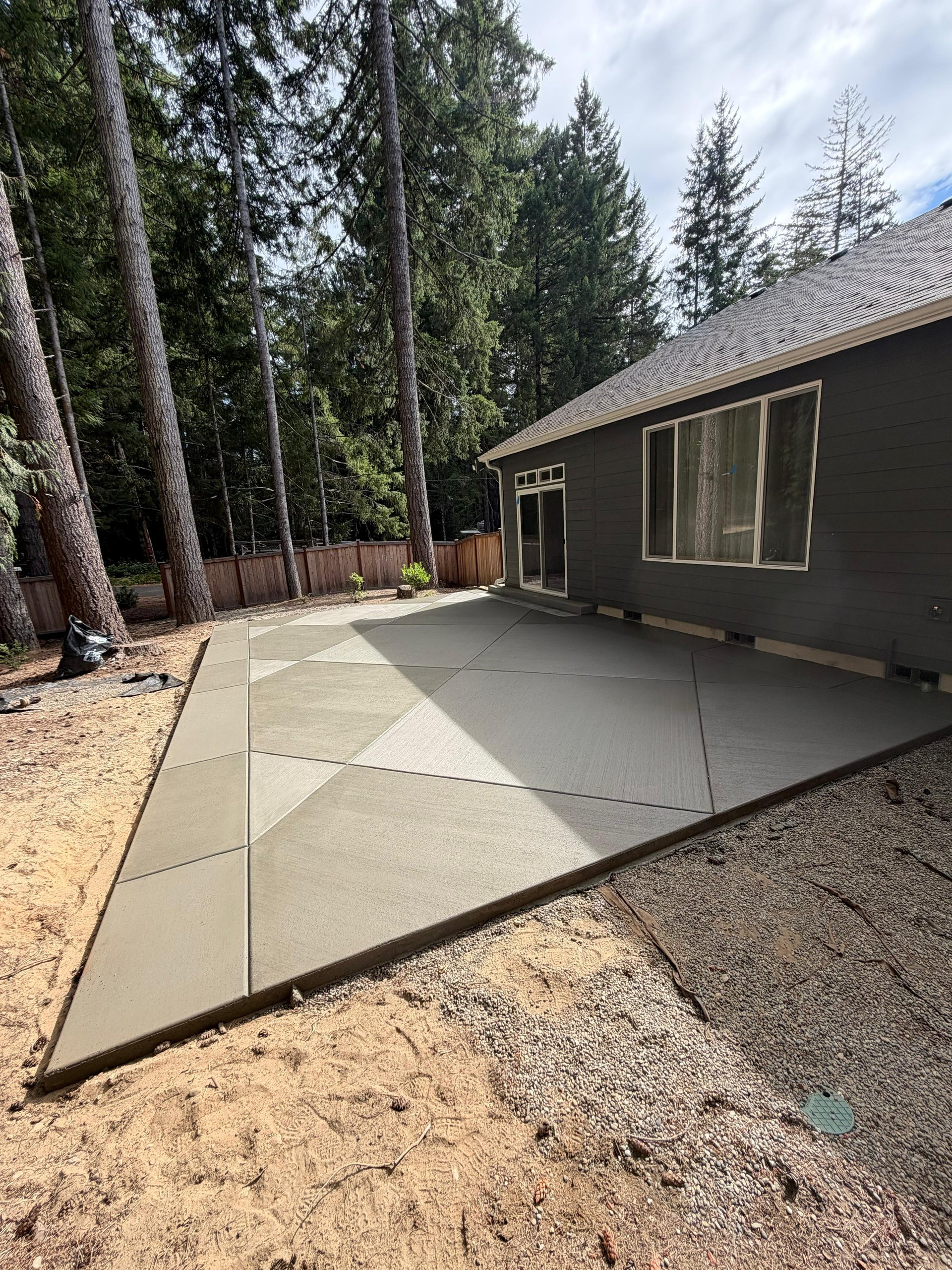 Modern dark cabin with newly poured concrete patio surrounded by tall evergreen trees