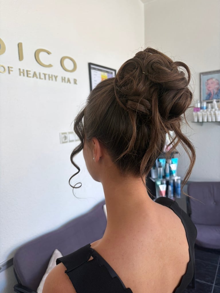 Back view of woman with brown hair styled in an updo with loose curls, seated in a salon setting