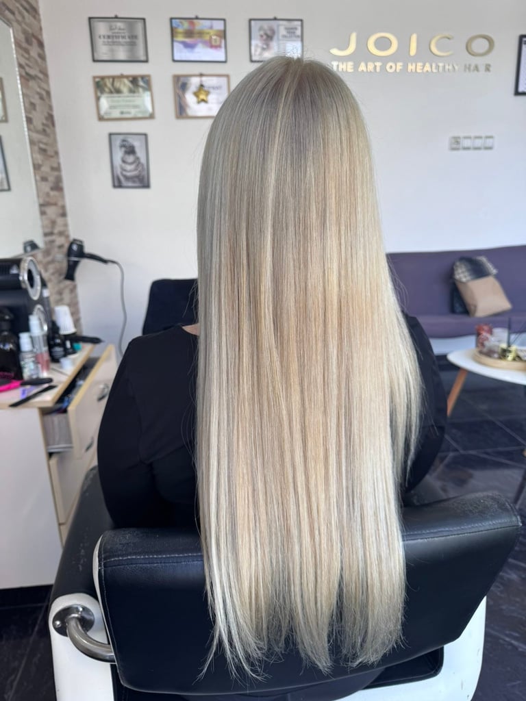 Person with long straight ash blonde hair viewed from behind in a salon chair with Joico signage visible on wall