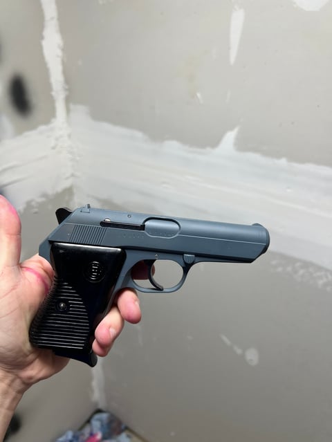 Person holding a black semi-automatic pistol in their hand against a white interior background