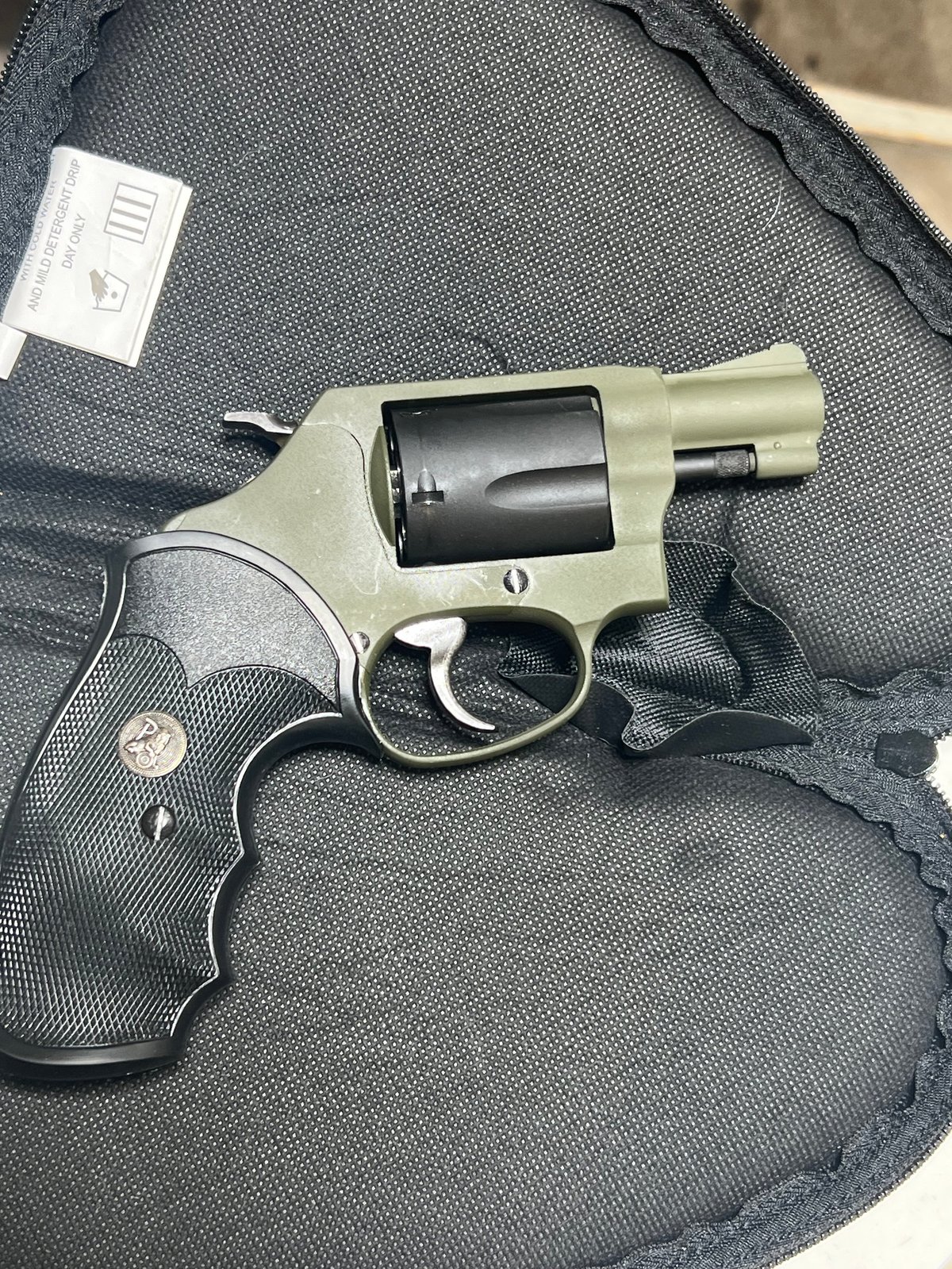 Silver and black revolver with black grips resting on gray fabric bag with care tag