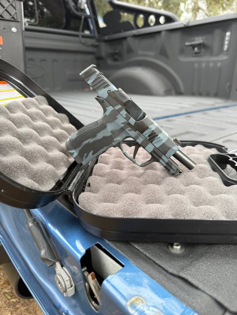 Stainless steel handgun resting on beige foam in the bed of a blue pickup truck