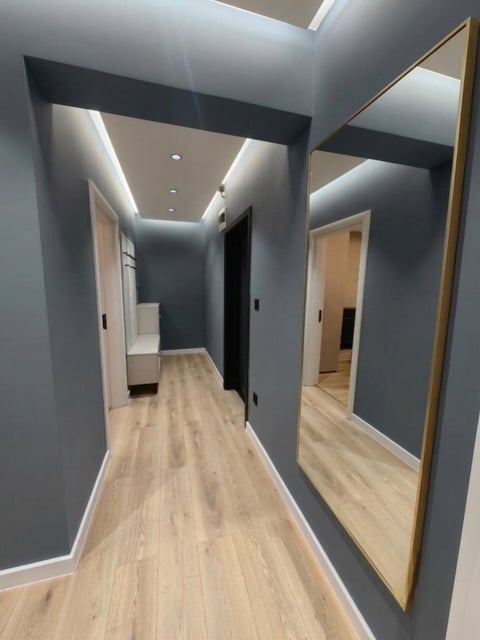 Modern hallway with gray walls, wooden flooring, recessed lighting, and mirrored doors leading to multiple rooms