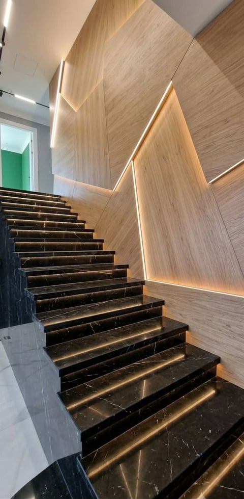 Modern staircase with black marble steps, warm wood-paneled walls, and integrated LED lighting throughout the stairwell