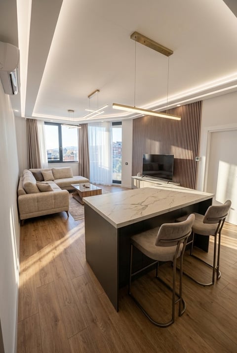 Modern open-plan apartment with beige sofa, kitchen island with bar seating, and city views through floor-to-ceiling windows
