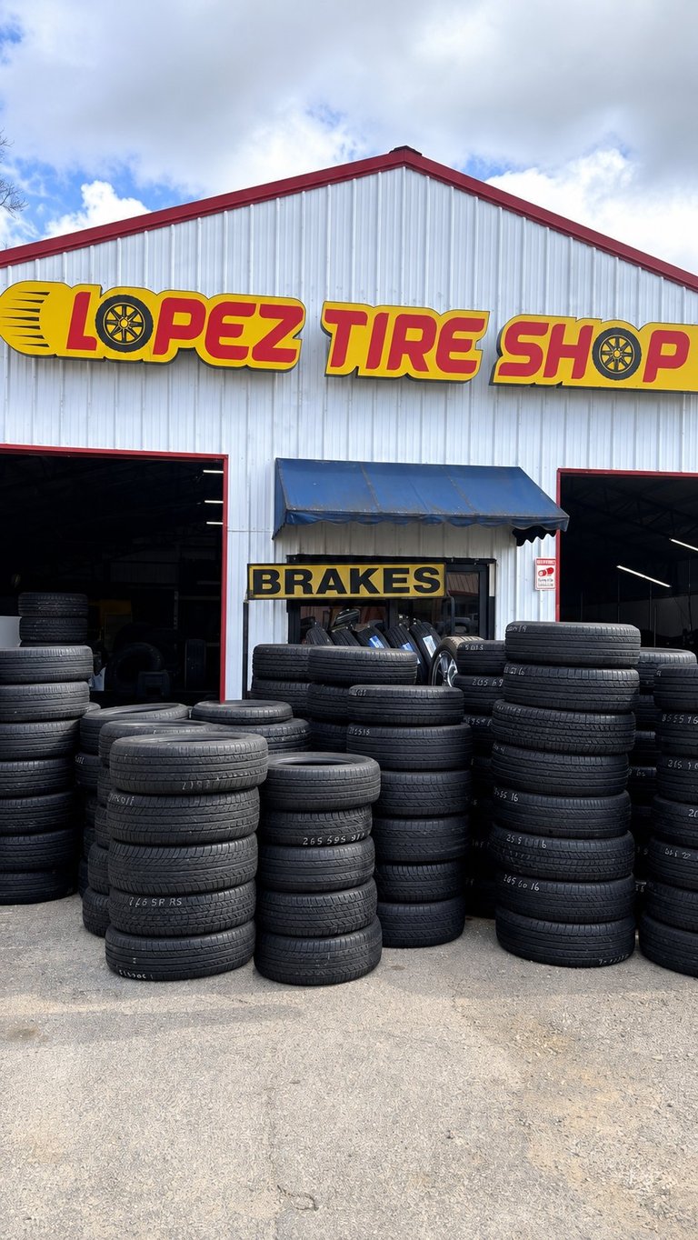 Lopez Tire Shop storefront with red and white metal building displaying large yellow signage and stacked used tires in front