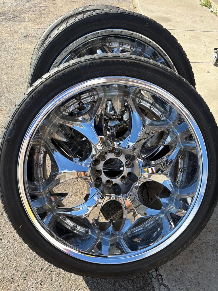 Two chrome and blue custom car wheels with black tires stacked on concrete pavement