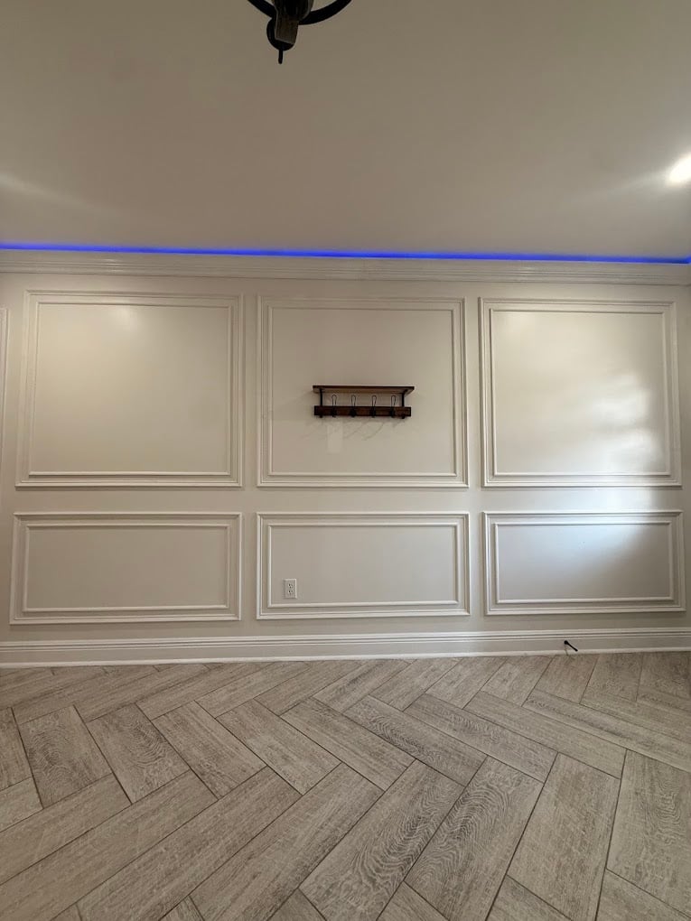 Modern room with white wainscoted walls, herringbone wood flooring, black ceiling fixture, and blue accent line above paneling