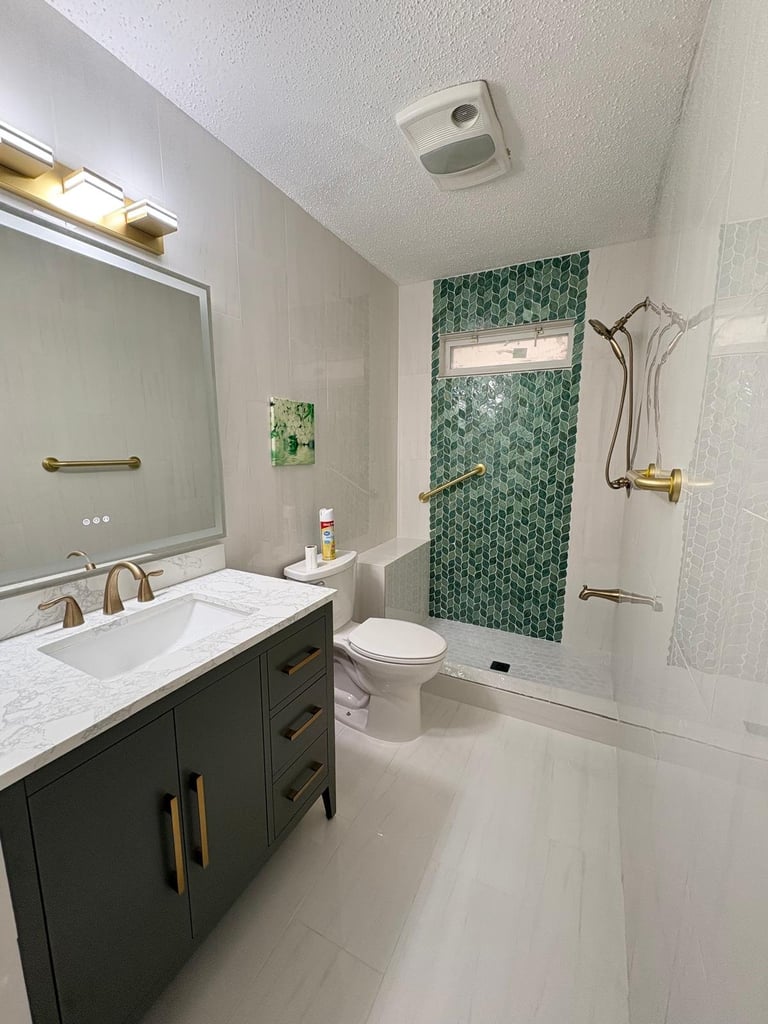 Modern bathroom with dark vanity, white countertop, large mirror, green hexagon tile shower accent, and brass fixtures