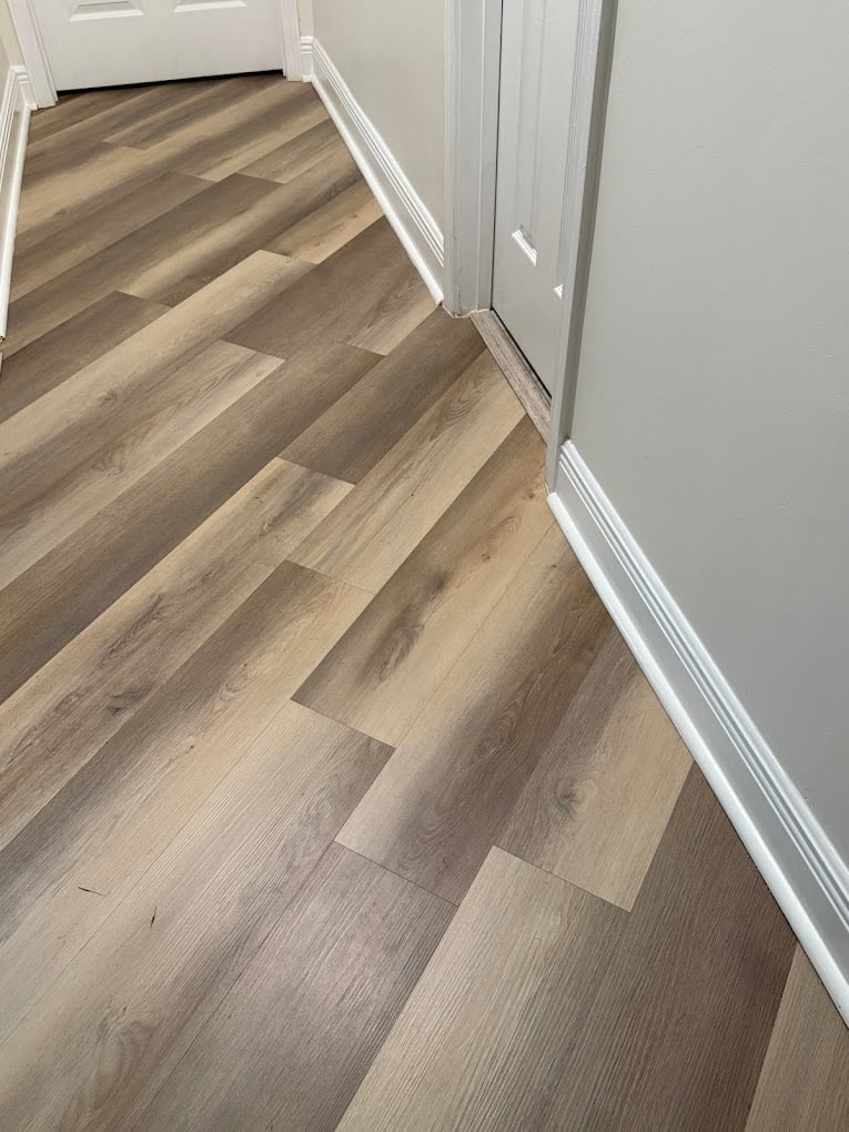 Hallway with light wood laminate flooring, white baseboards, and light gray walls