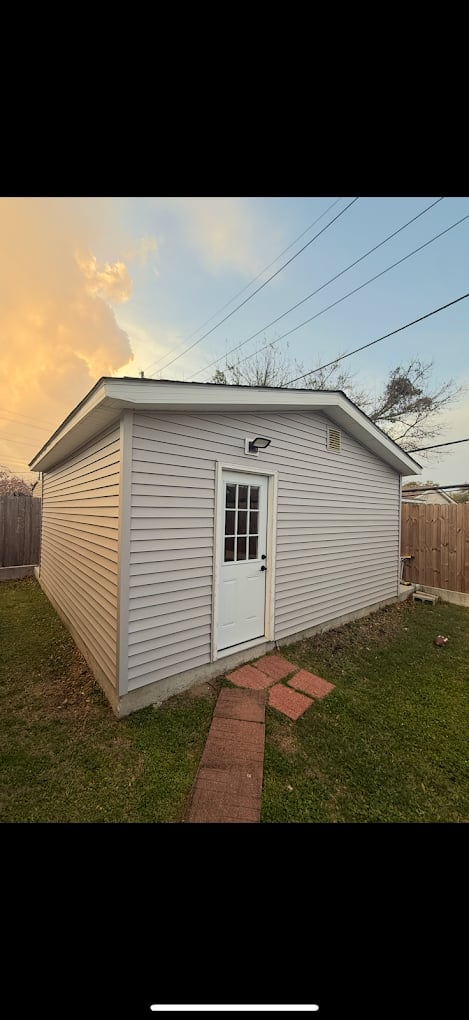 White vinyl-sided storage shed with single door in backyard during sunset, power lines visible overhead