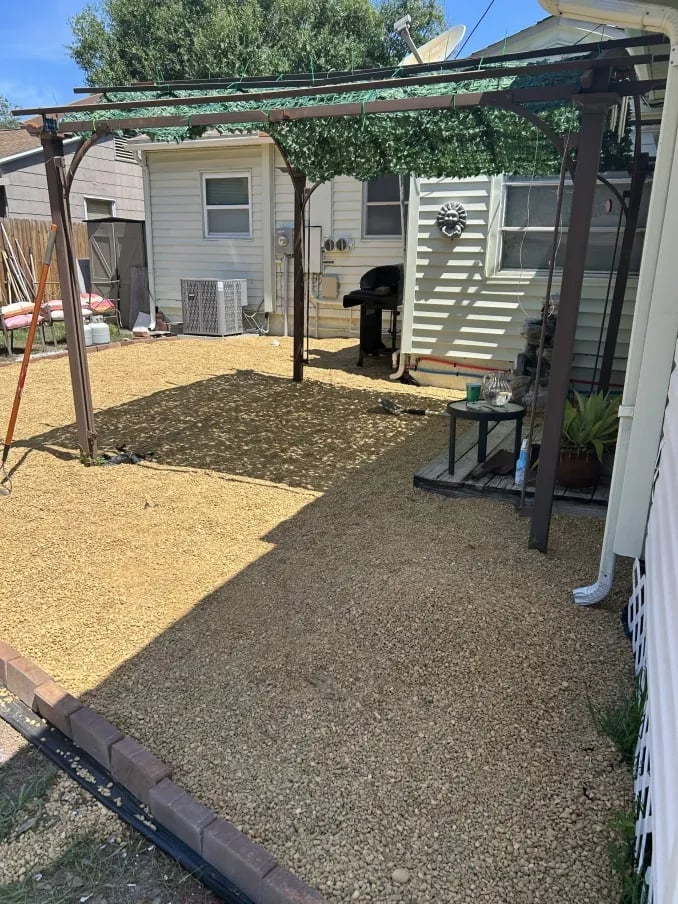 Backyard patio with metal pergola, gravel ground, and small residential house with white siding