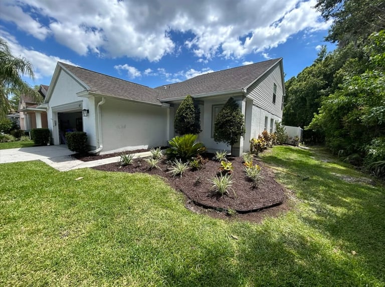 White single-story house with attached garage, manicured landscaping, and green lawn on a sunny day with blue sky